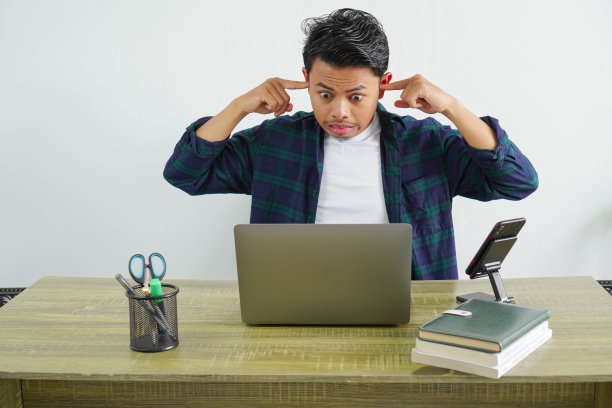 一位亚洲商人坐在工作场所捂着耳朵图片下载