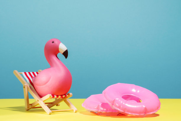 可爱的粉红色火烈鸟坐在沙滩椅上，蓝色和黄色的背景。副本的空间。图片下载