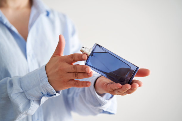 穿着蓝色衬衫的手拿着一瓶蓝色的香水。图片下载