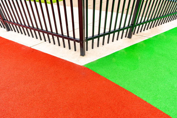 一个装饰性的黑色金属栅栏围绕着一个多颜色的操场表面的特写照片。图片下载