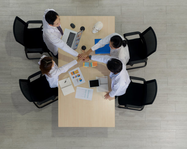 四名医疗专业人员会面的高角度照片。他们穿着白大褂，通常与医生、研究人员、科学家或实验室技术人员等医护人员有关。图片下载