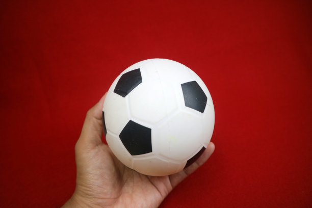 一只手拿着一个黑白相间的小玩具橡皮球。红色的背景图片下载