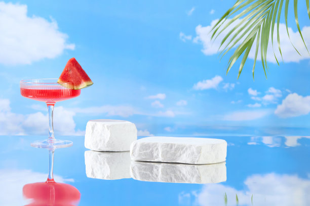 蓝天背景照片与夏天的概念，从正面看，两个石膏基座放置在玻璃表面的中心，旁边的鸡尾酒杯含有红色的西瓜汁。设计空间图片下载
