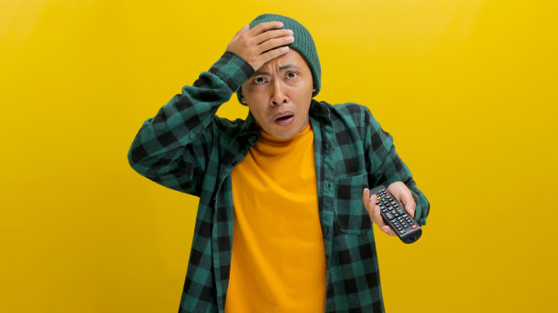 不开心的亚洲年轻人拿着电视遥控器摸着自己的头图片下载