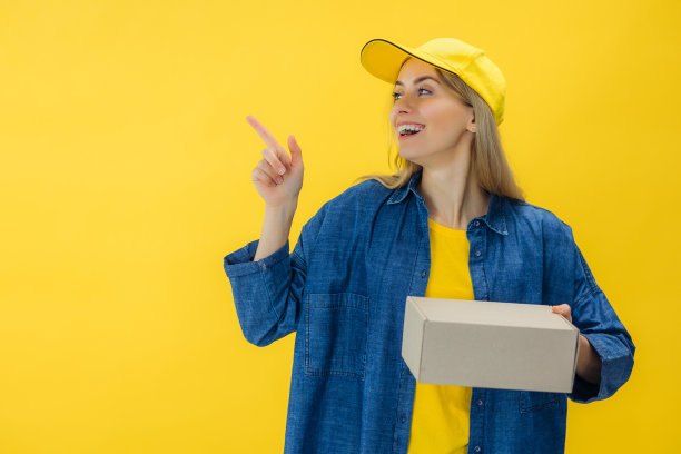 微笑的年轻女子手里拿着盒子指着复印空间。积极的女快递员送包裹。专业服务理念。图片下载