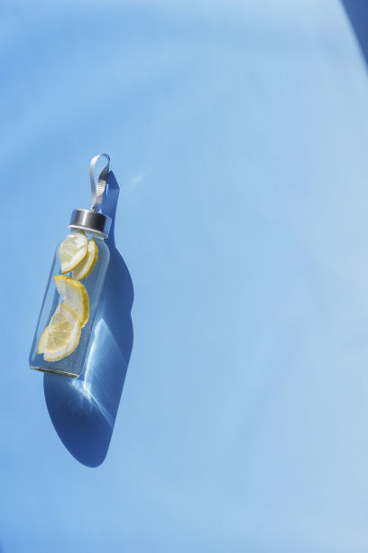 柠檬水喝排毒瓶，硬阴影在阳光下蓝色的背景。养生、饮食、饮食健康的理念。顶景玻璃可重复使用的水瓶，环保的生活方式，最小的照片图片下载