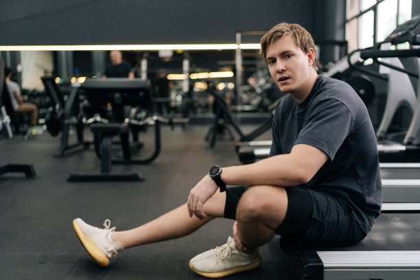 筋疲力尽的跑步者在健身房休息的肖像，坐在跑步机上。筋疲力尽、汗流浃背的男性在有氧运动后呼吸困难的照片。图片下载