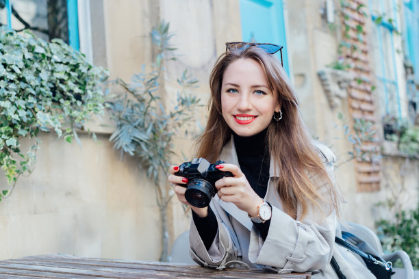 快乐微笑的女游客的肖像，在旅游城市散步后，坐在咖啡馆露台的桌子上休息，看着数码相机上的照片。旅游博主、摄影师、网红捕捉这一刻。图片下载