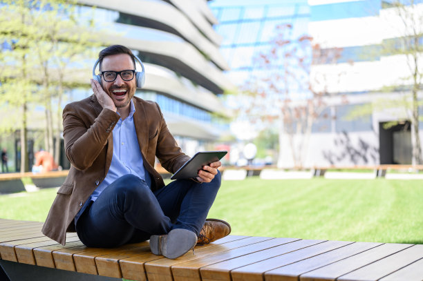 开朗的年轻专业人士戴着耳机，在长凳上用数码平板电脑参加在线会议图片下载