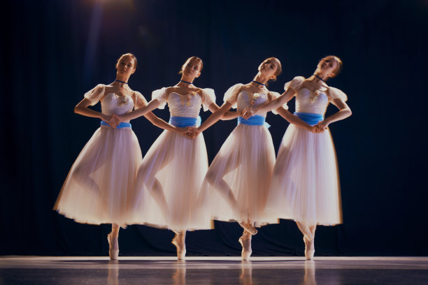 迷人的年轻女孩，穿着白色芭蕾舞裙，戴着蓝色蝴蝶结的芭蕾舞演员在舞台上跳着足尖舞。照片与运动模糊效果图片下载