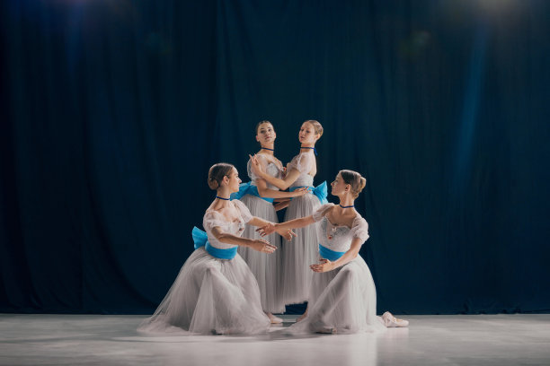 四个年轻的舞者穿着美丽的白色和蓝色芭蕾舞服，在舞台上摆出各种优雅的姿势。当代艺术。图片下载