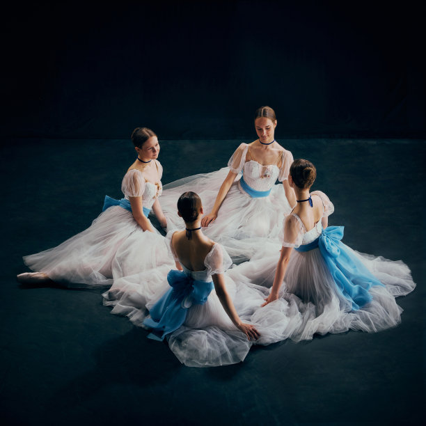四个年轻的芭蕾舞演员优雅地围成一个圈坐着，白色的芭蕾舞裙上装饰着飘逸的蓝色腰带。图片下载