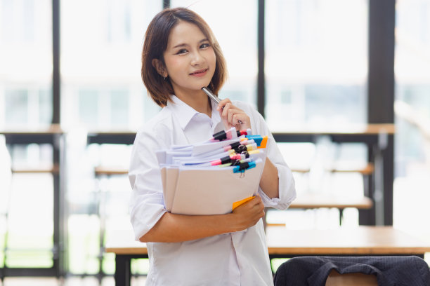 迷人的亚洲女商人，在办公室的桌子上与成堆的文件一起工作。图片下载