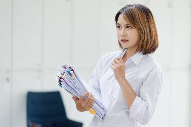 迷人的亚洲女商人，在办公室的桌子上与成堆的文件一起工作。图片下载