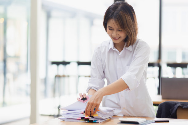 迷人的亚洲女商人，在办公室的桌子上与成堆的文件一起工作。图片下载