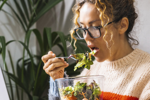 正在节食的女人一边在家里用笔记本电脑看在线节目，一边用透明的碗吃新鲜的沙拉。年轻的企业家忙于新的商业概念生活方式在线。午休时间女士图片下载