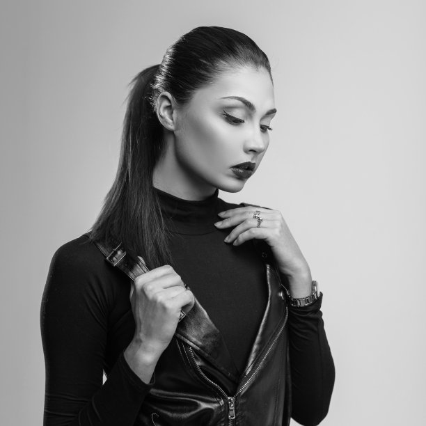 时尚美丽的年轻女性模特，优雅的发型，性感的嘴唇，穿着时尚的皮衣，在房间里的复古墙上摆姿势。迷人的黑发女孩。时尚的黑白照片。图片下载