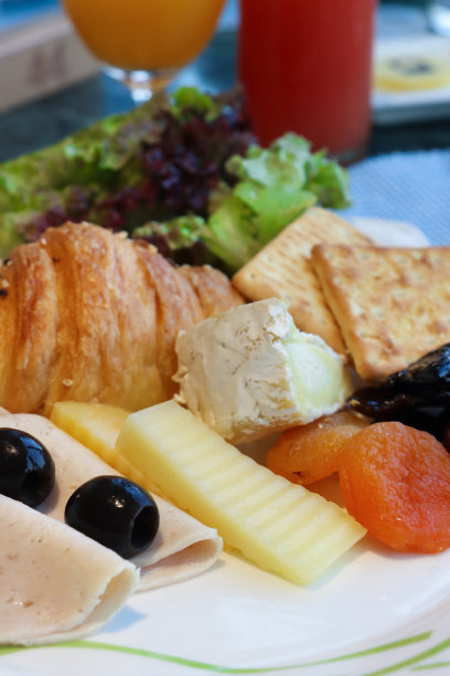 白色盘子的特写图片，里面装着酒店自助早餐的食材，自助欧陆式早餐，羊角面包，干饼干，布里干酪，切达干酪，鸡肉火腿，杏干，黑橄榄，生菜叶，一杯果汁图片下载