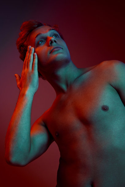 低角度的照片，年轻有吸引力的摆姿势赤膊展示他完美的身体在霓虹灯渐变的红色背景。图片下载