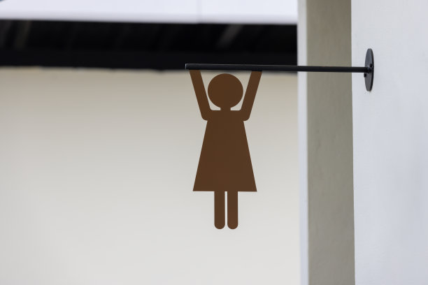 一个女人正吊在一块牌子上。这个标志是棕色的，有一个女厕所。图片下载