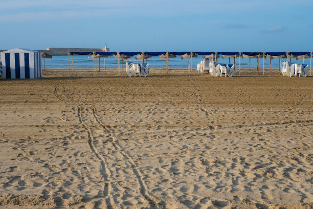 在空旷的沙滩上，一排排的椅子和遮阳伞挡住了阳光。早....。沙滩上的脚印。图片下载