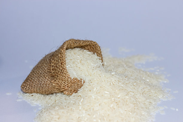 泰国的茉莉花米。白色的茉莉花米的图片放在麻袋和勺子在白色的背景。图片下载