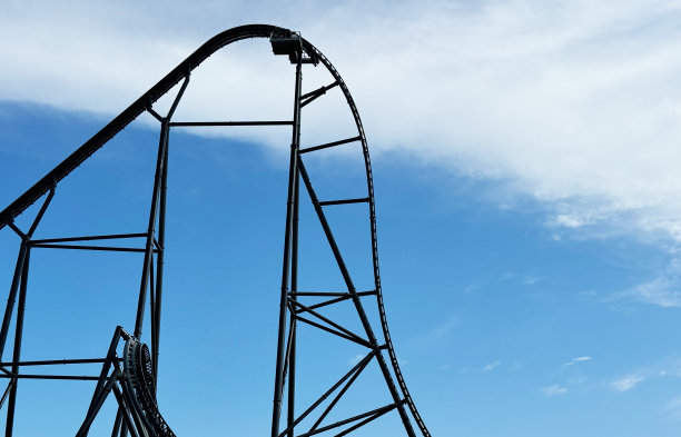 一个巨大的黑色过山车，有一个大落差。孤立在蓝天上，有一些云。图片下载