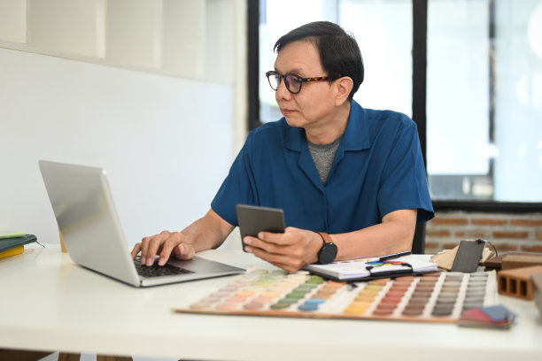 成熟的室内设计师使用笔记本电脑和工作与材料和颜色样品在他的工作场所图片下载