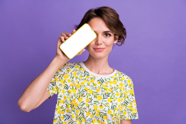 漂亮的年轻女子的肖像遮住眼睛空的空间手机屏幕穿t恤孤立的紫色背景图片下载