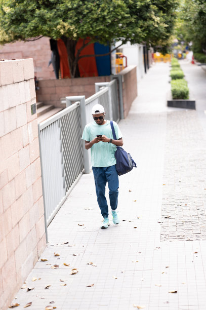 一个放松的男人走在街上，正在使用智能手机图片下载