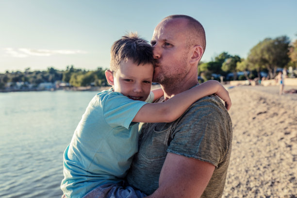 微笑的男孩和他爸爸在海滩的照片。图片下载