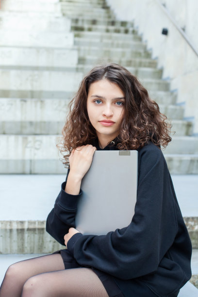 照片中，一位美丽的卷发少女在城市的街道上使用笔记本电脑。图片下载