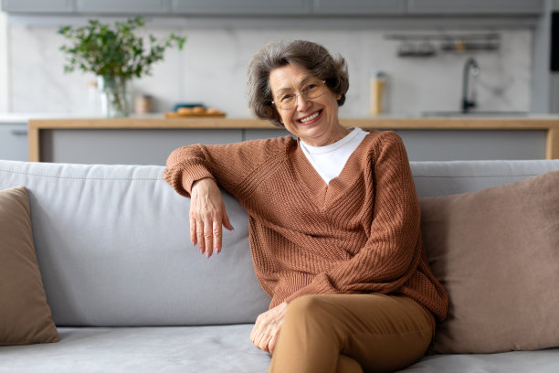 快乐的老夫人躺在沙发上，对着镜头微笑，在客厅享受居家的舒适，自由的空间图片下载