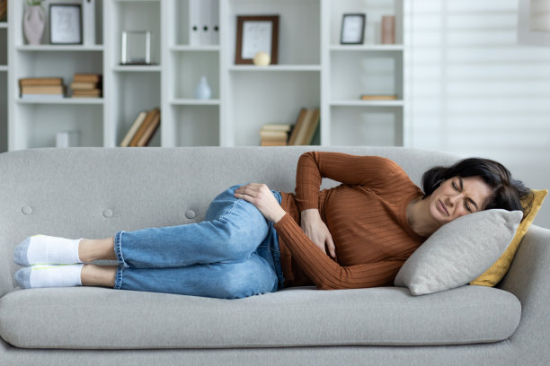 一个痛苦的女人躺在家里的沙发上捂着肚子图片下载