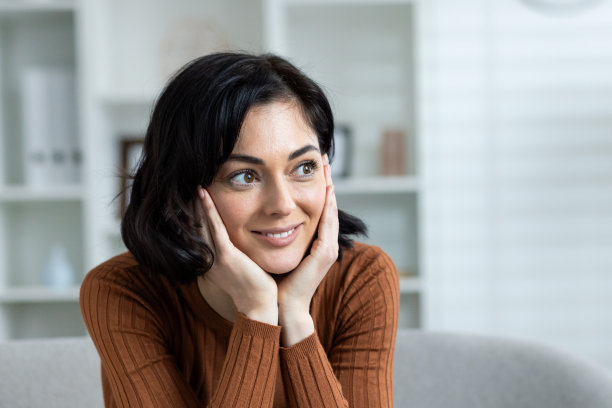 一个年轻的女人坐在家里的沙发上微笑的特写照片。双手抱着头，恍惚地望向一旁图片下载