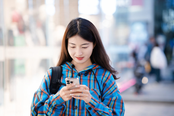 年轻的亚洲女子晚上在城市街道上使用智能手机图片下载
