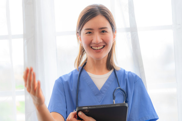 亚洲女性医疗助理，白色背景的智能平板电脑。在医院工作的成熟女护士画像。妇女保健工作者。一个漂亮的年轻护士的画像。图片下载