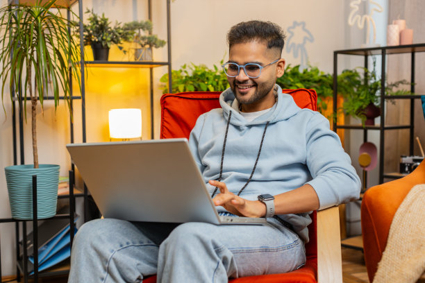 年轻的自由职业者坐在椅子上工作的笔记本电脑浏览互联网在家里的客厅图片下载