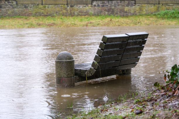 城市中的洪水:由于连续下雨而被淹没的步行区，城市中的长椅，河岸，垃圾箱，树木和护柱图片下载