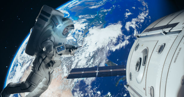 年轻的宇航员漂浮在零重力的太空中。宇航员在轨道航天器外的开放空间使用笔记本电脑，浏览卫星维修工作的说明手册图片下载