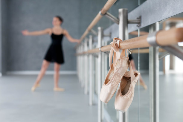 尖头鞋挂在芭蕾舞杠上。芭蕾舞演员练习的模糊背景。女孩在古典舞蹈学校进行舞蹈锻炼和练习。图片下载