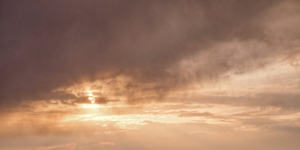 这张照片显示了多云的天空，太阳透过云层，在乌云中投射出温暖的光芒。图片下载