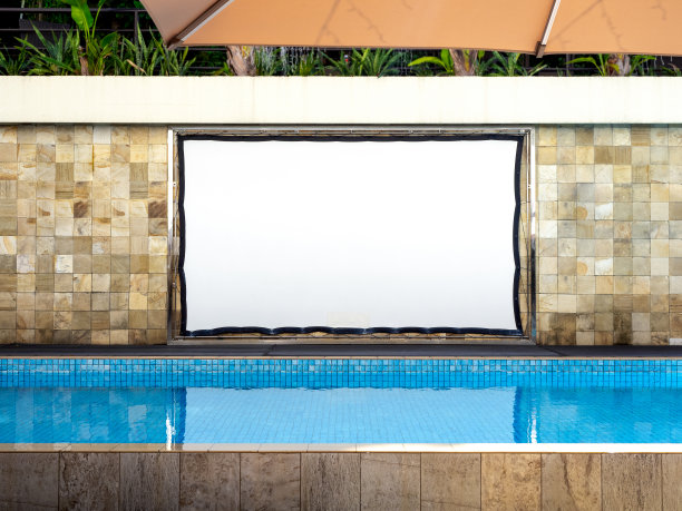 游泳池附近的瓷砖墙面背景上悬挂的空白白色大型户外防水投影仪屏幕。泳池边空荡荡的放映机，一个人也没有。图片下载