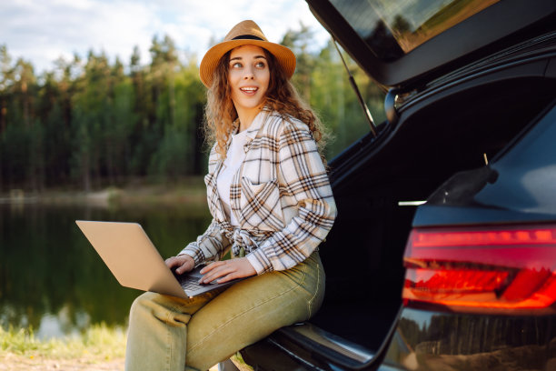 年轻女子坐在汽车后备箱里使用笔记本电脑。图片下载