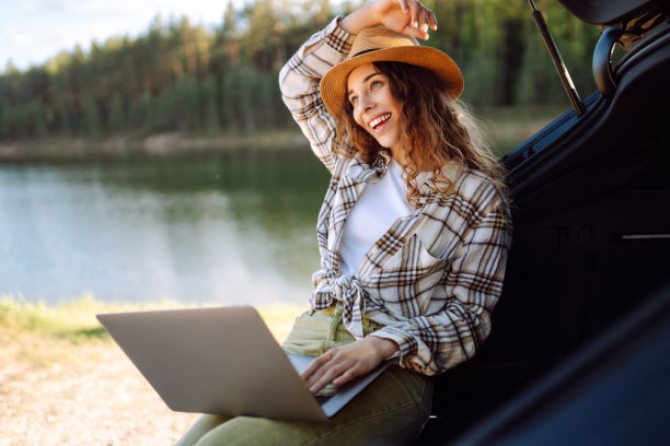 年轻女子坐在汽车后备箱里使用笔记本电脑。图片下载