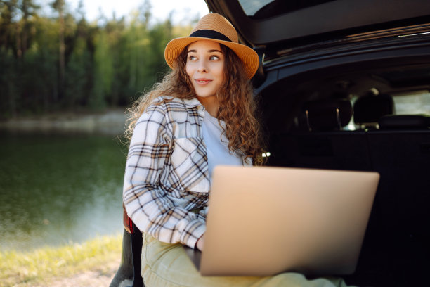 年轻女子坐在汽车后备箱里使用笔记本电脑。图片下载