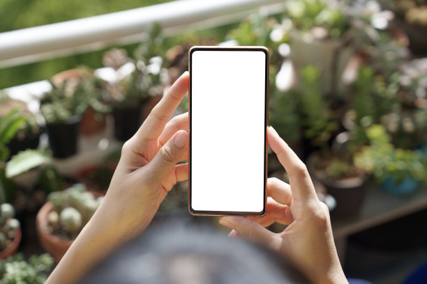 在这张裁剪过的图片中，一名亚洲女子放松地坐在花园后院的野餐椅上，使用着一部空白屏幕的智能手机。图片下载