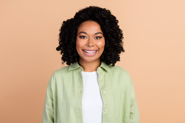 照片中漂亮的年轻女子笑容满面，穿着绿色衬衫，衬托在米色背景上图片下载