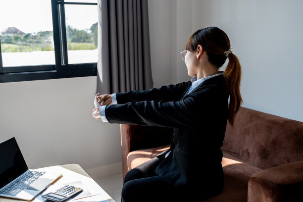 一位成功的女商人在家里办公室的沙发上长时间对着笔记本电脑辛苦工作后，感到身体疼痛并伸展自己，办公室综合症概念图片下载