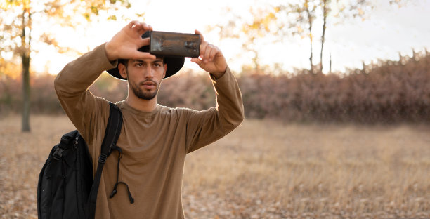 男子摄影师与背包和手机拍摄照片的秋天风景旅游。生活方式的爱好图片下载